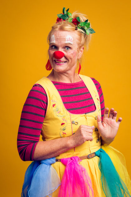 Erwachsene Person mit roter Clownsnase trägt ein gestreiftes Oberteil und ein buntes Kleid.